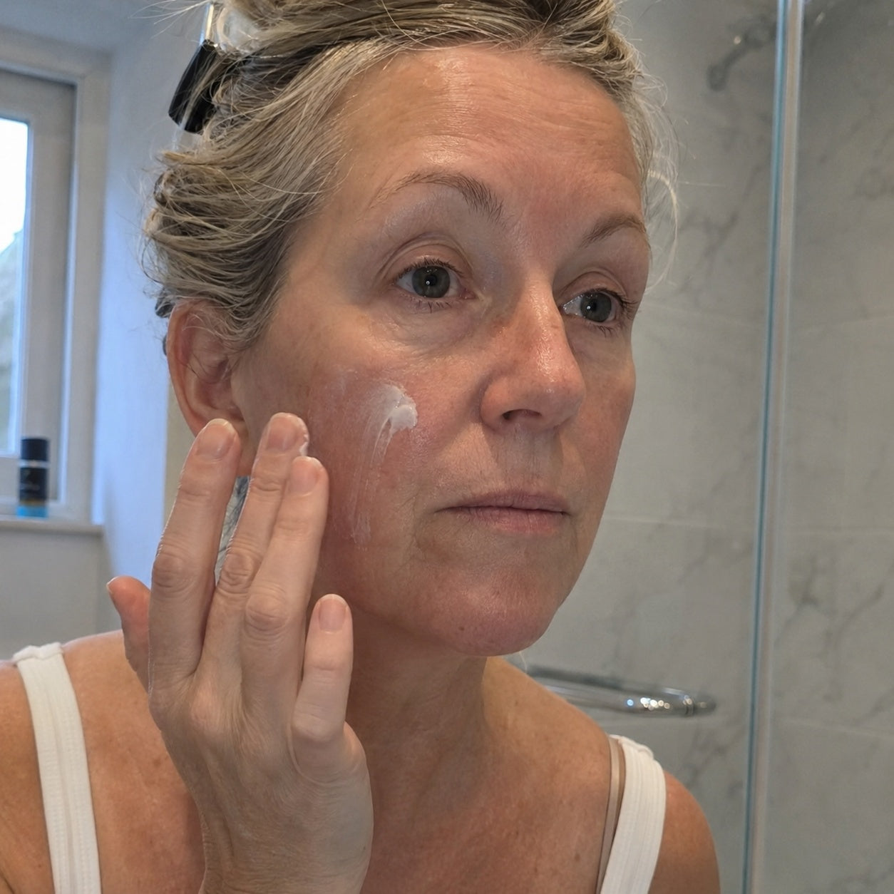 A woman over 45 applying the all-in-one cream in natural light